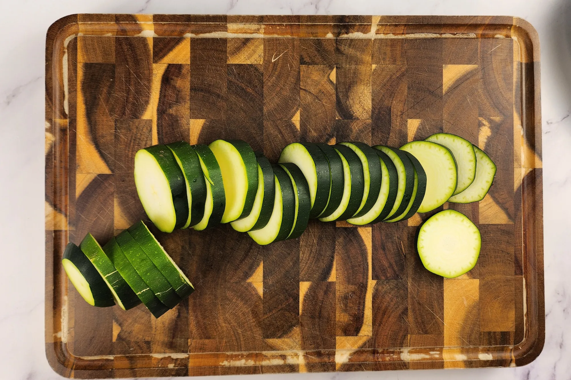 Slices of zucchinis on a wooden chopping board.