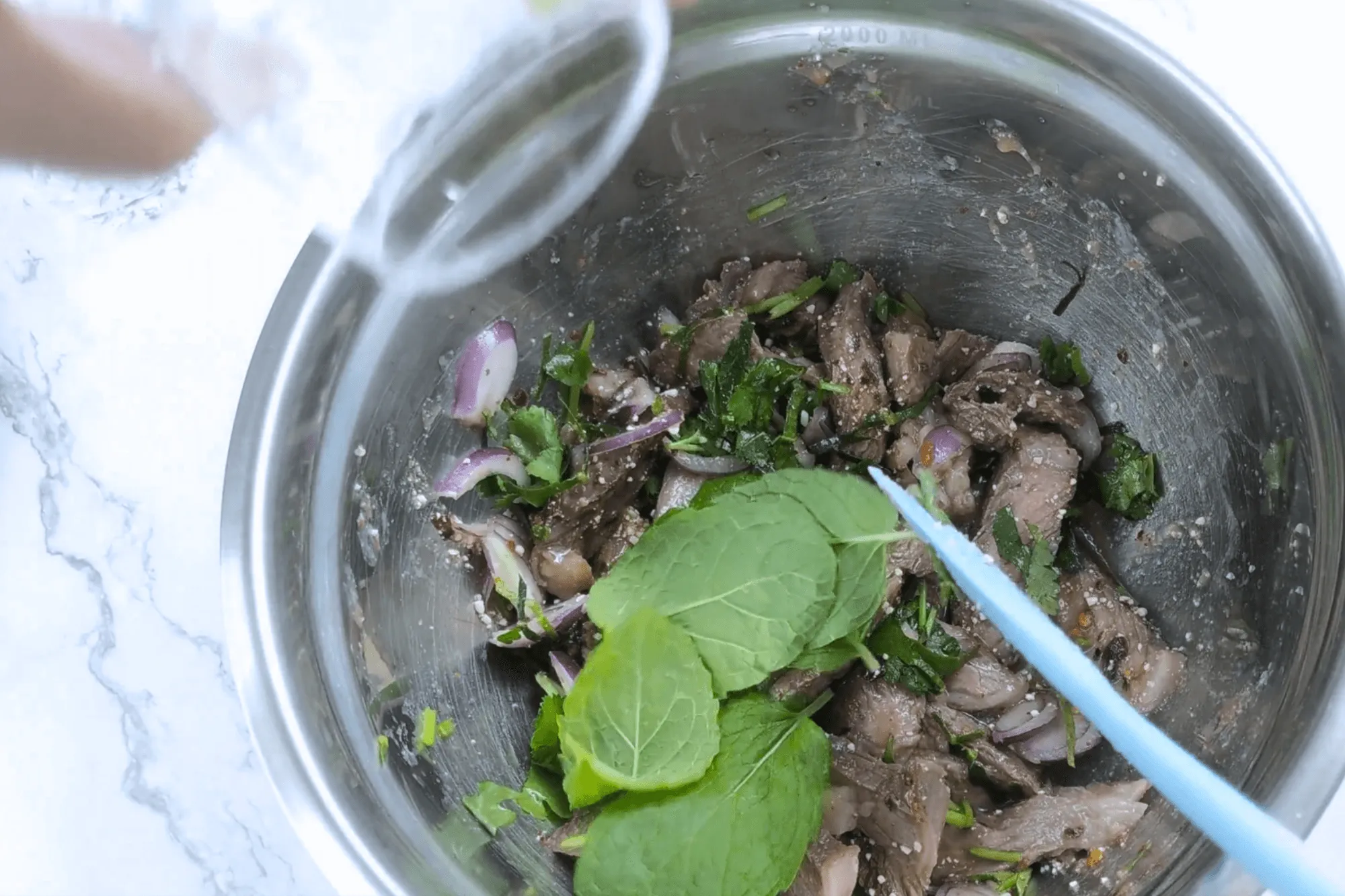 Add sliced shallots, chopped coriander, mint leaves, and sliced kaffir lime leaves. Plate and serve immediately.