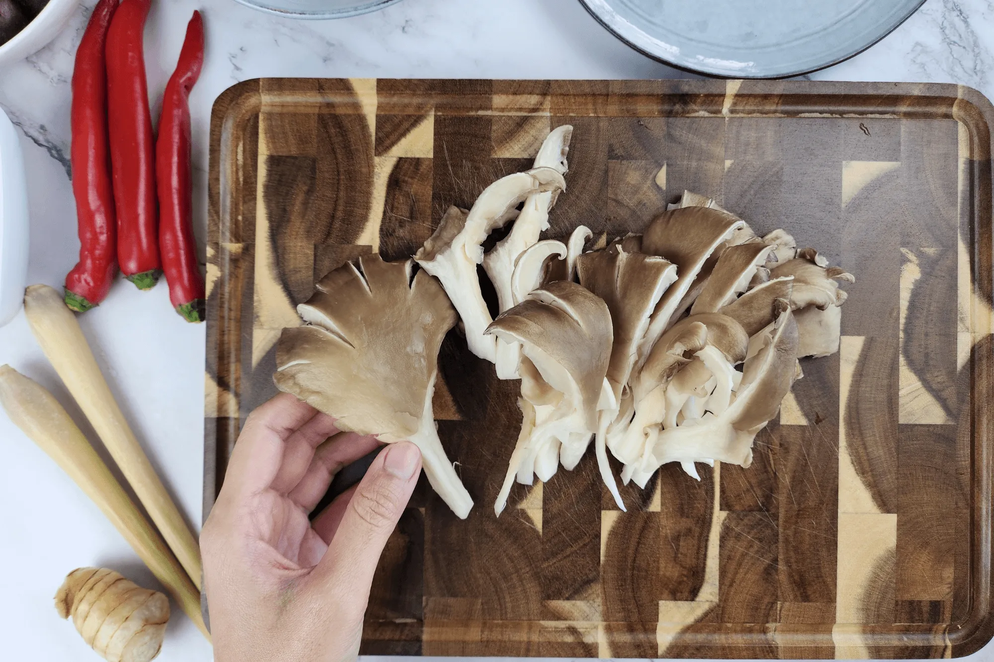 Trim the roots or stems of the oyster mushrooms and tear them into bite-sized pieces. Cut the lemongrass diagonally into short or long sections, then bruise it lightly using a pestle or the back of a knife to release its aroma. Slice the young galangal into thin rounds. Tear the kaffir lime leaves by hand. Peel the shallots and crush them gently to release their flavor.